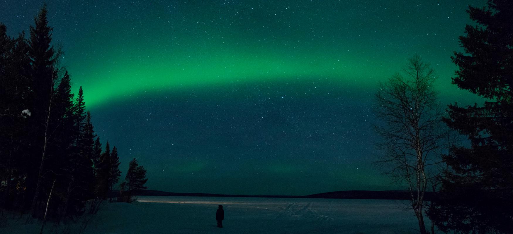 Tourist standing at night looking up at the northern lights.