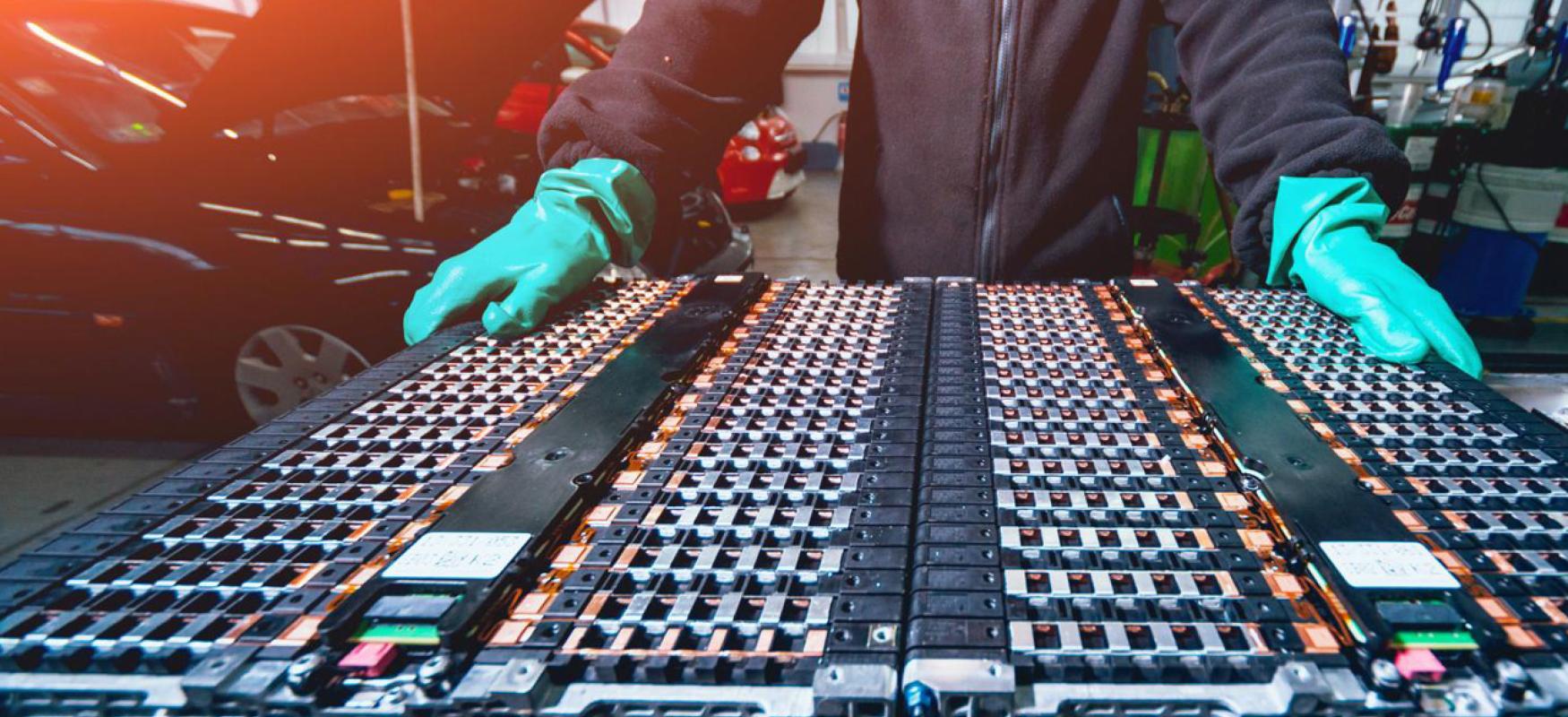Mechanic standing nest to many electrical vechicle batteries