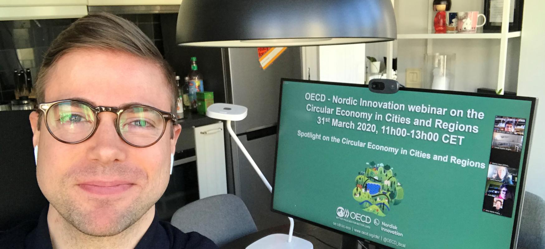 Senior innovation adviser at Nordic Innovation, Elis benediktsson in front of a computer screen displaying an image of the OECD and Nordic Innovation webinar 31 march 2020