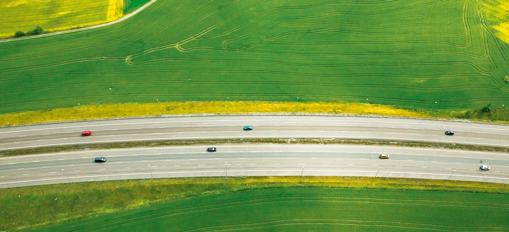 Aerial view of a road going through a green field.